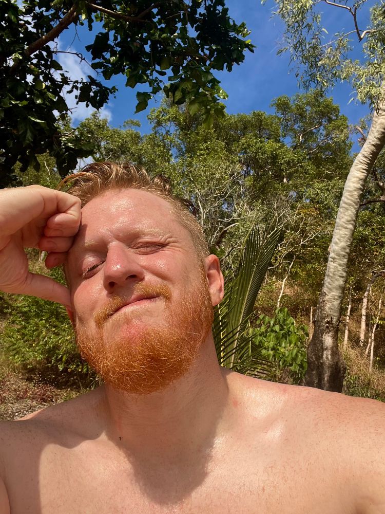 Ginger man nude at the beach squinting into the sun as he takes in the vitamin D
