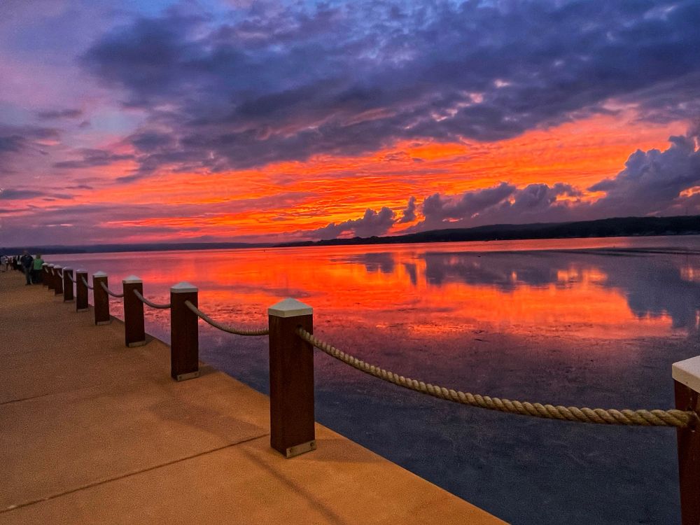 A colorful sky; with hues or orange and violet, is reflected on the calm waters of a lake.