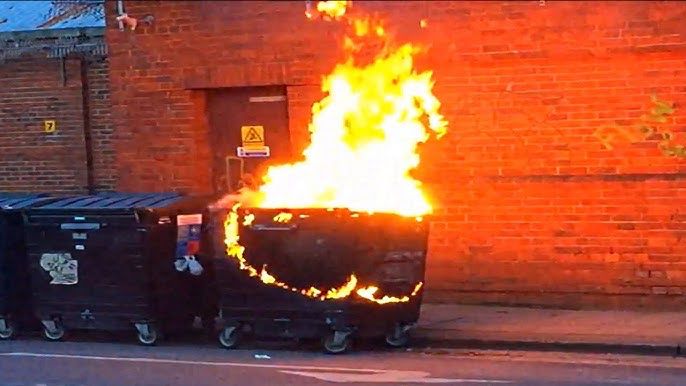 A large black street bin flamingly on fire