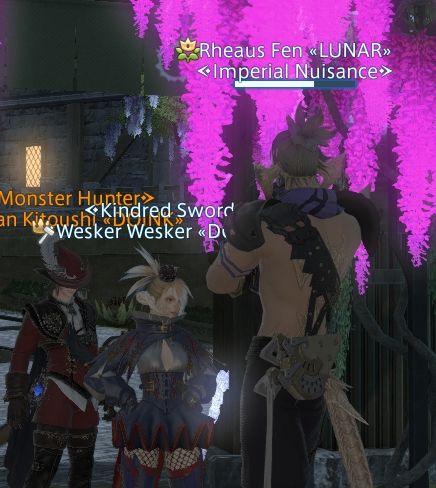 Photo of three wols standing in front of a bright pink lilac tree. Rheaus has his back to the camera and is facing the other two. He towers over them in height. 