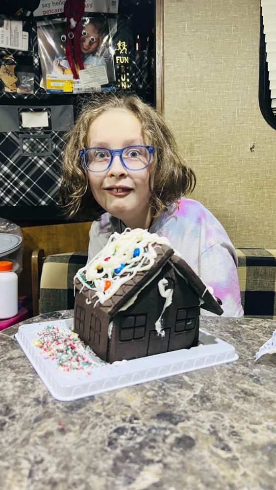 R is all about funny faces these days and they've got wide eyes and raised eyebrows with teeth showing through a goofy smile. The M&M gingerbread house was built sideways on the tray, so the walkway leads to a wall with only windows, and the whole thing is covered in white icing.