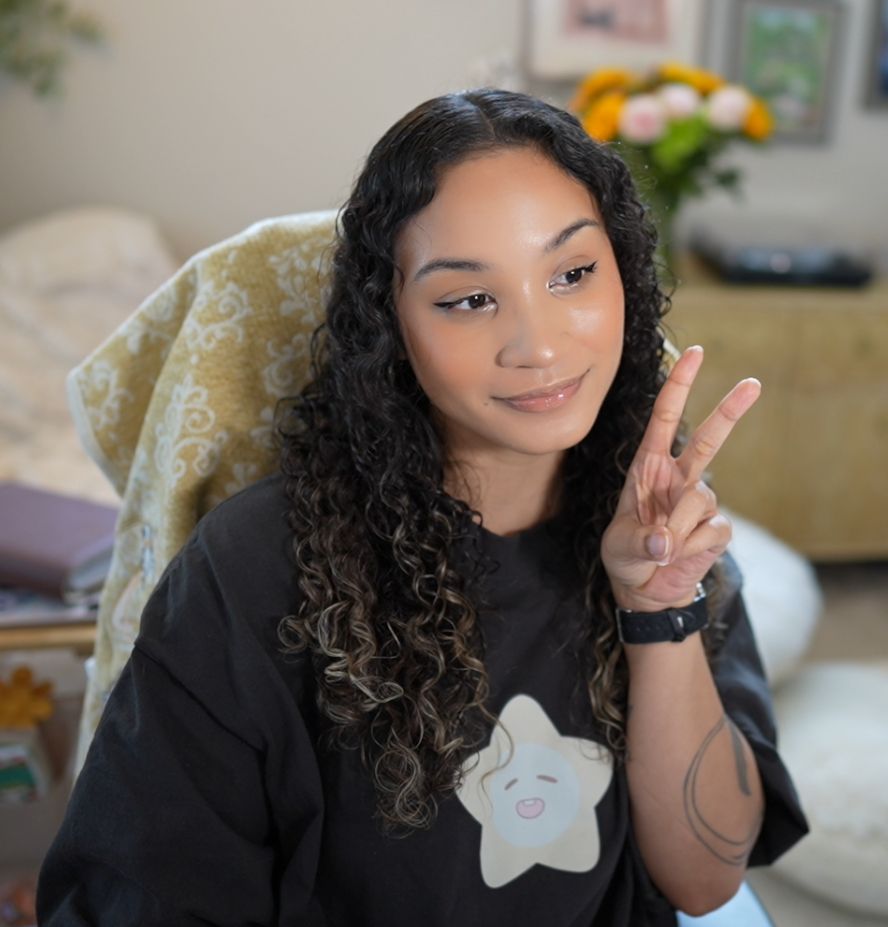 lorie doing a peace sign wearing a xavier from love and deepspace shirt 