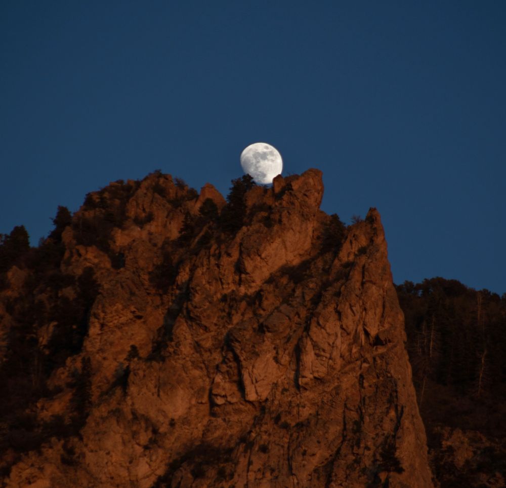 A gibbous moon rises over a rugged cliff bathed in sunset light. Photo: Bill Dunford