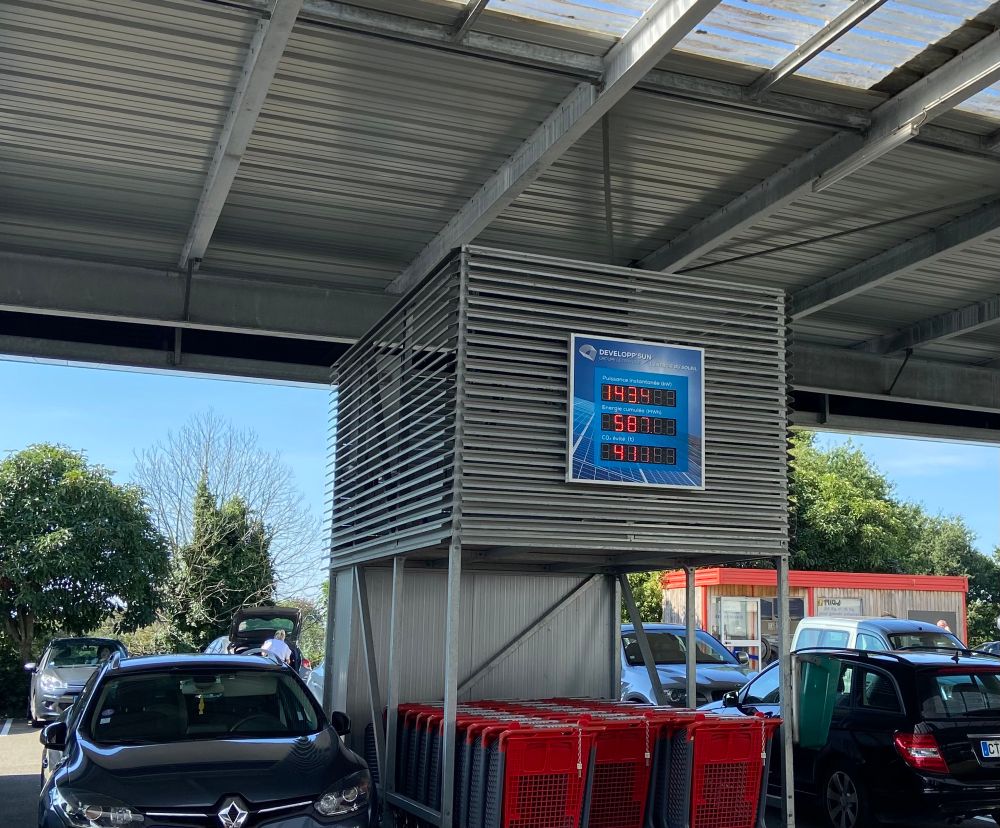 Display in French supermarket car park. Shows how much energy is being generated by the solar panels on the roof above. Instantaneous kWh, cumulative MWh and tonnes of CO2 mitigated.