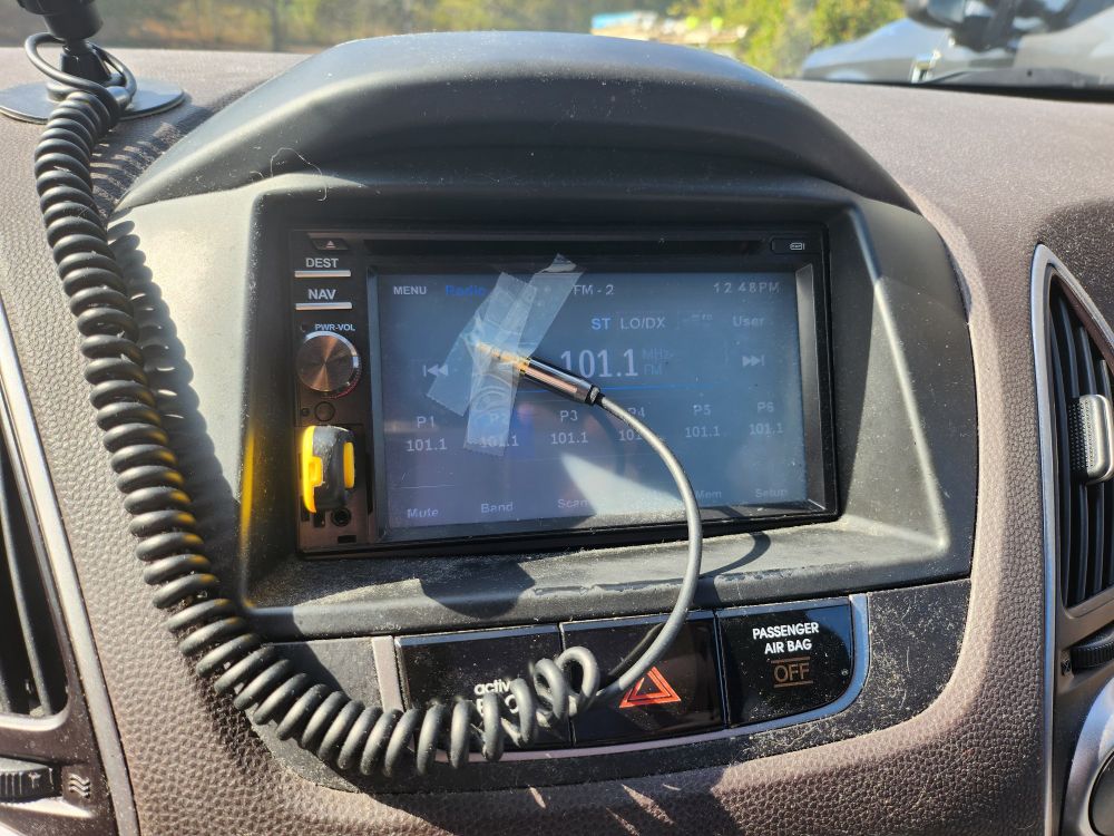 A touchscreen car radio with the end of an audio cable taped to the screen.