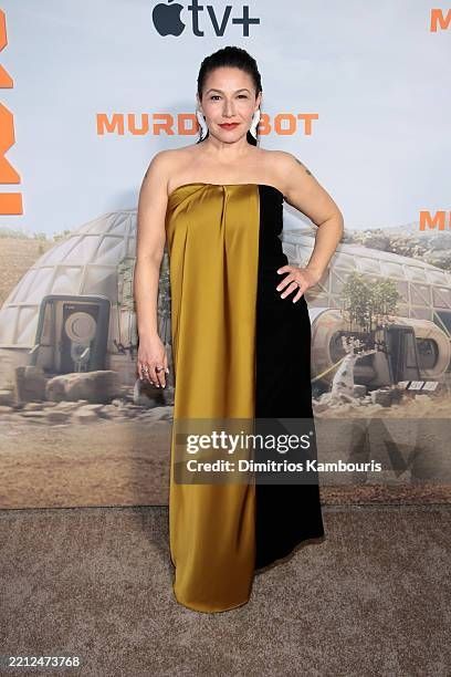 Tamara Podemski posing on the Murderbot red carpet in a gorgeous color-block gold and black strapless gown. She has large white earrings that look like feathers possibly. Stunning!
