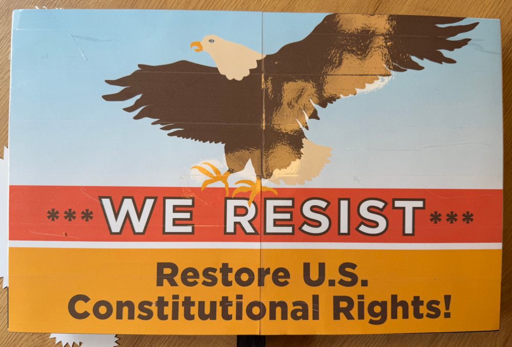 Sign showing an eagle landing on top of words: “We resist. Restore U.S. constitutional rights.”