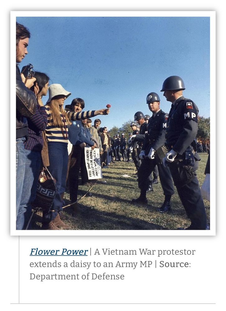 Photo of 1967 anti-Vietnam-war protesters with one young woman holding out a flower to Army MP officer. 
