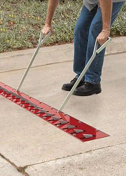 Someone uses a tool to raise or lower the teeth of a traffic-arresting device embedded into the pavement 