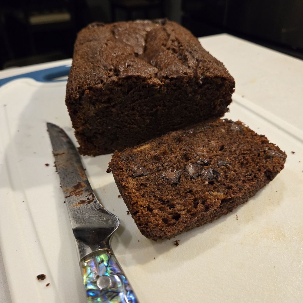 dark chocolate banana bread, sliced, on a cutting board with a knife near by. 
