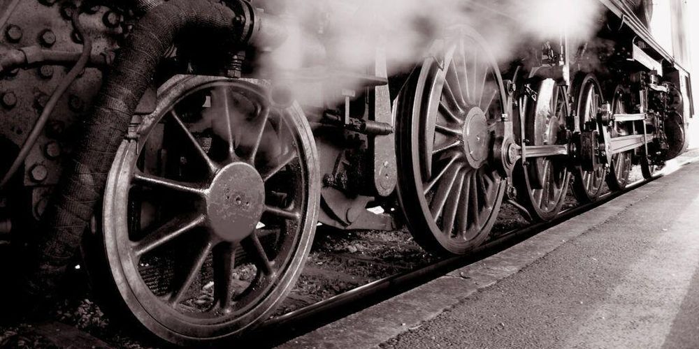 Locomotora de vapor checa fotografiada desde abajo y atrás, por el costado derecho, hacia adelante con un ángulo bastante cerrado. Se aprecian seis ruedas, de las que las cuatro centrales son tractoras, unidas por bielas. Fotografía en blanco y negro.