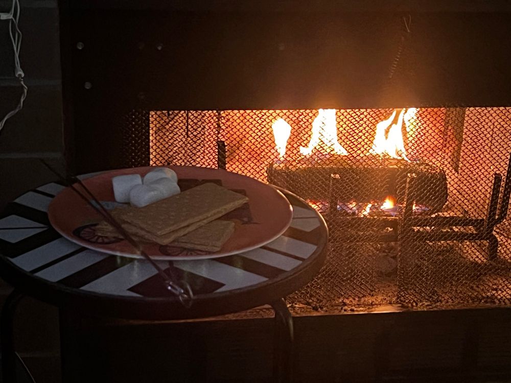 Photo of a plate with smores ingredients on it in front of a fire place