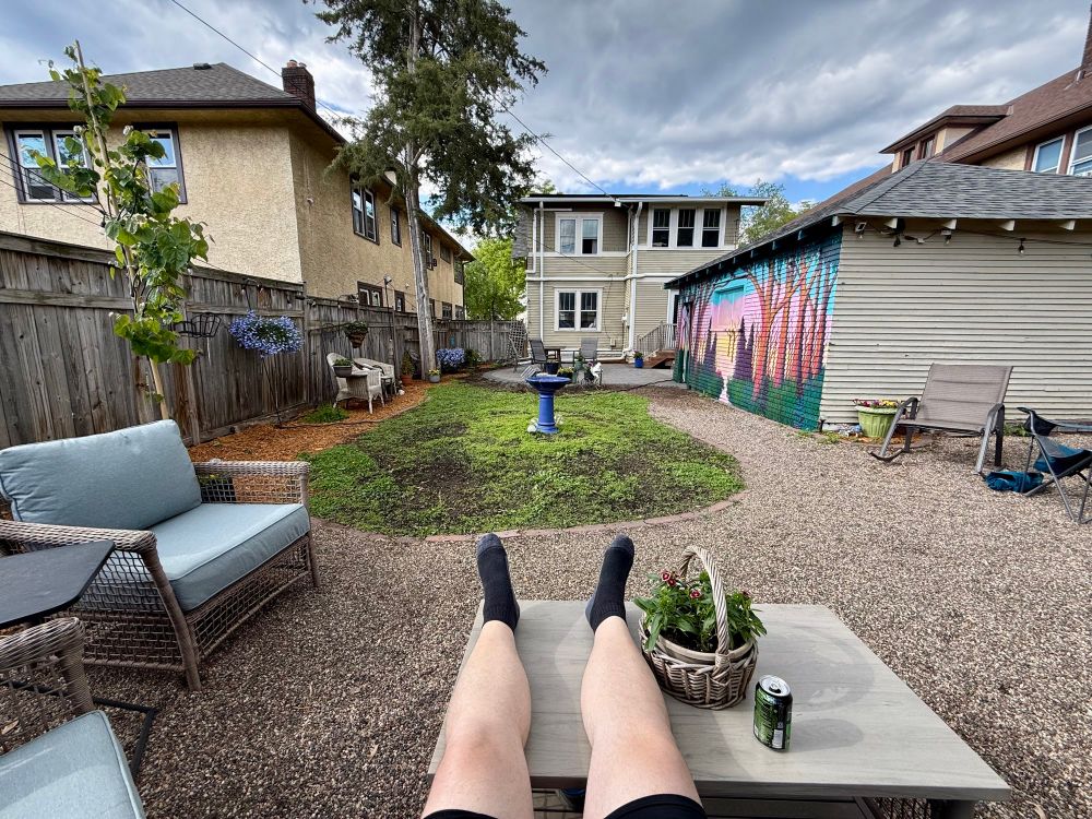 A relaxing backyard scene with a man’s legs propped up on a table in the foreground 
