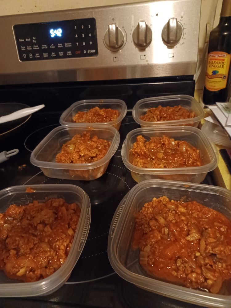 Six plastic containers on a range top half-filled with bolognese sauce