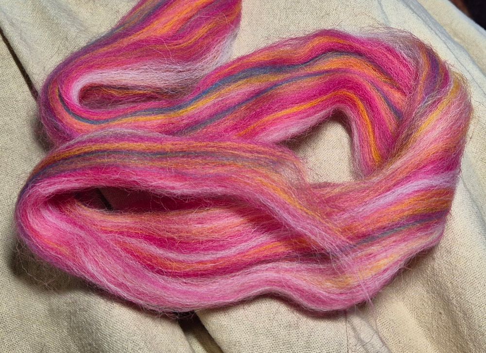 A hank of mostly pink fibre, there is also white, yellow, and green fibre shot through the pink, set against a cream background.