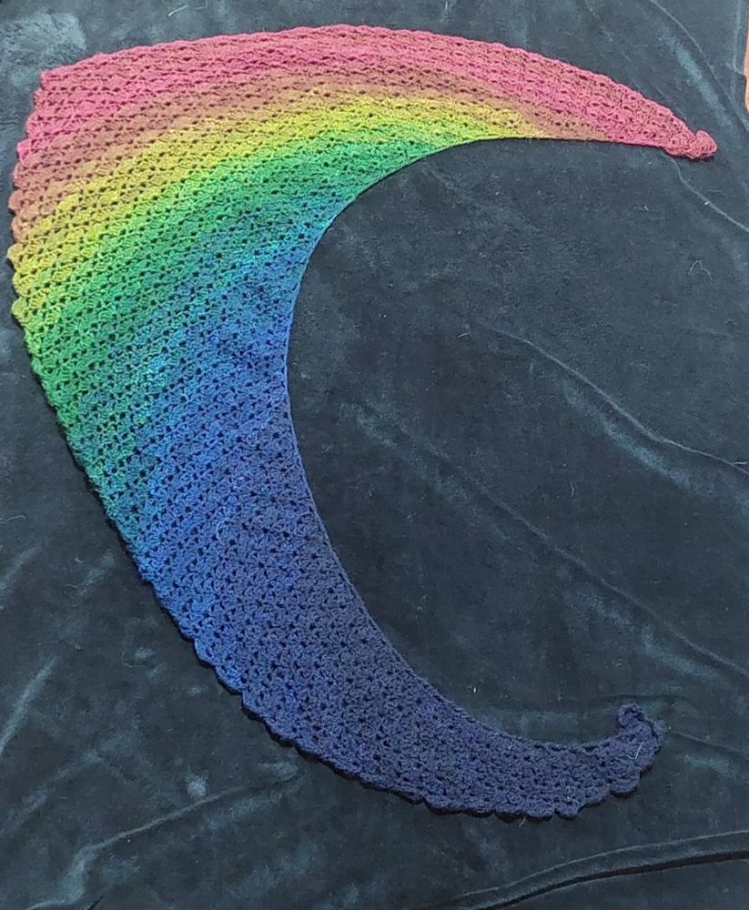 Rainbow coloured handspun crochet shawl set against a black background 