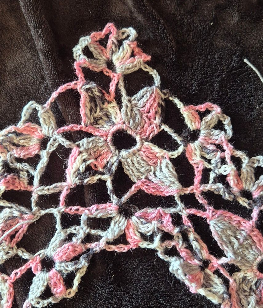 A pink, grey and black yarn, coloured crocheted motif set against a back background 