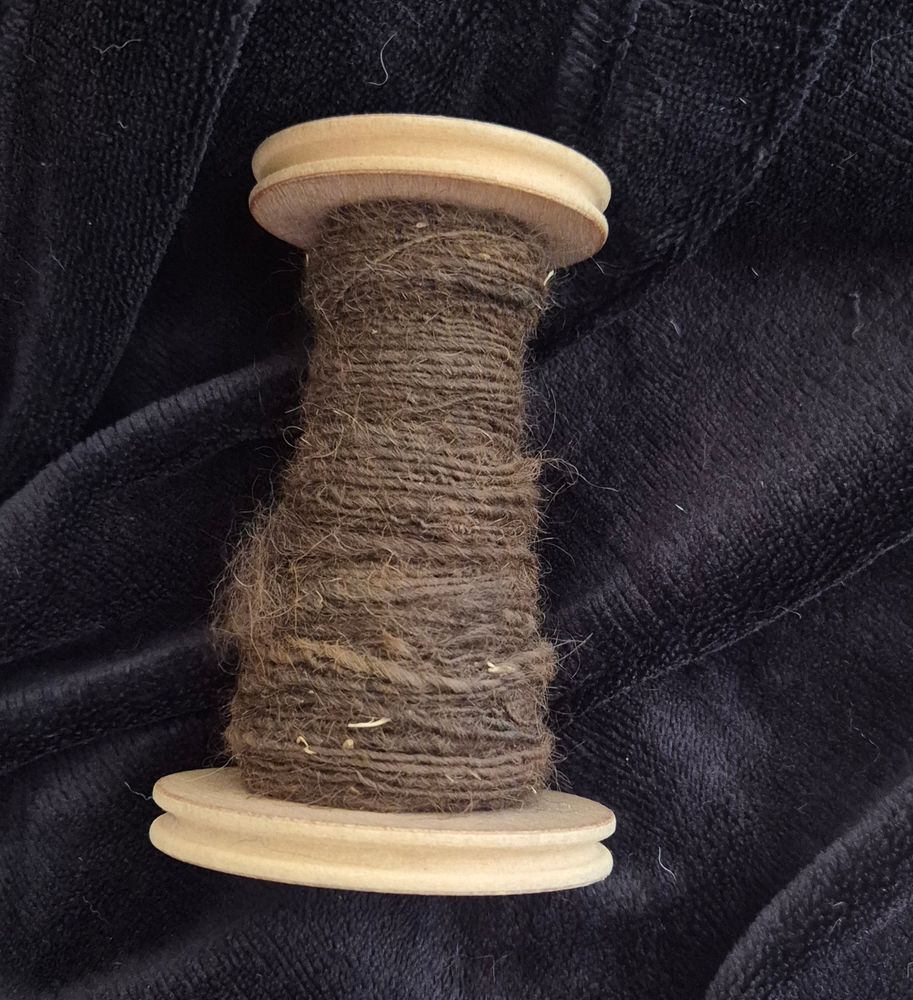 One bobbin with some brown handspun alpaca on it set against a black background. The handspun brown yarn looks a little dusty.