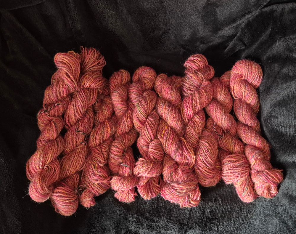 Nine skeins of the handspun pink mix yarn set against a black background 