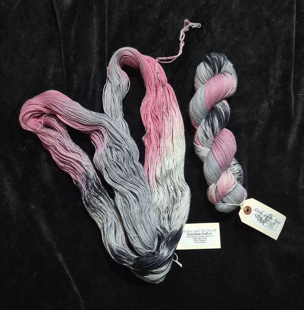 Two skeins of pink, white, grey and black coloured yarn. In the picture, one skein is loosely skeined and one skein is tightly skeined in a plait type of effect.
