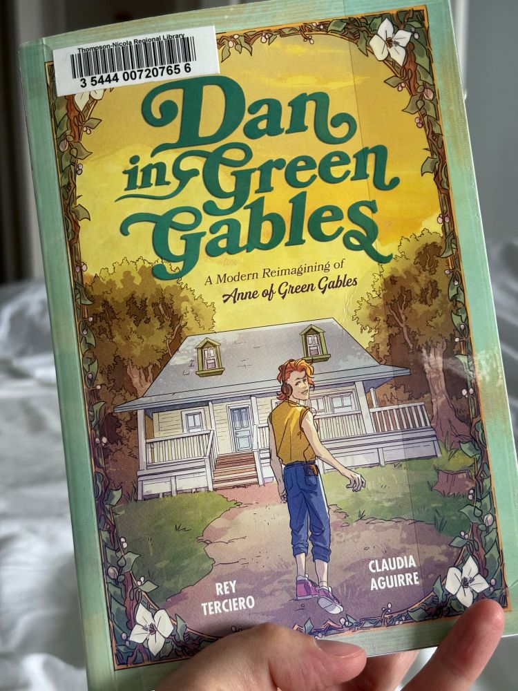 The cover of DAN IN GREEN GABLES shows a young white man with ginger hair dressed in blue capris and a yellow sleeveless shirt. He is looking over his shoulder at the camera, situated in front of a green-gabled home. 