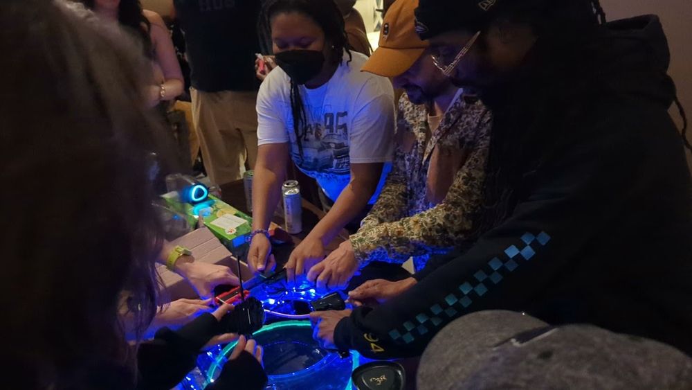 A group of people around a led-rimmed Beyblade arena, sending tops to battle.