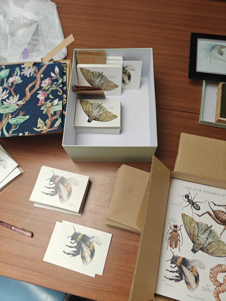 Picture of a table showing an assortment of watercolour art prints and greeting cards by Dorian, and packaging materials.