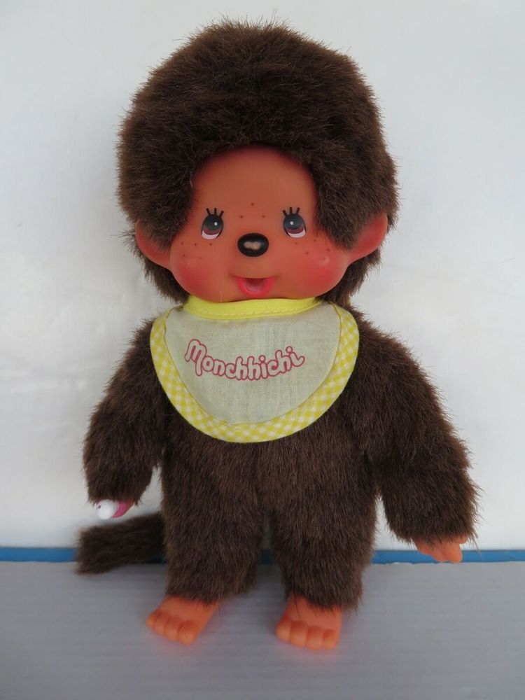 A monchichi doll on a white background. It has a yellow bib.