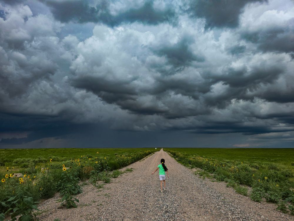 A road and a storm with a girl walking on the road