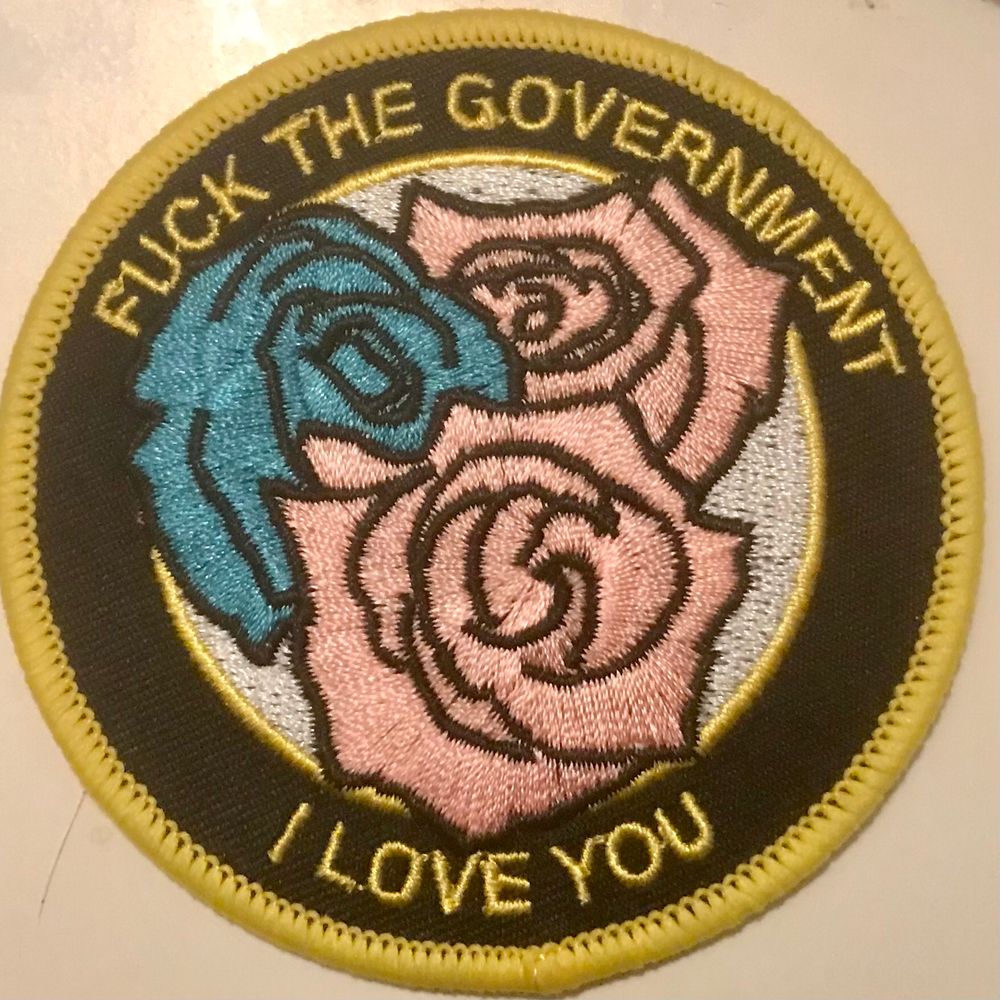 Sew on badge that reads ‘fuck the government, I love you’ with trans pride flag colours