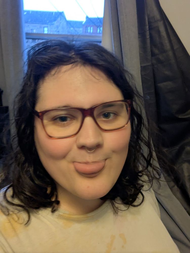 Picture of a black-haired woman in solid-frame glasses, a nose ring, and her tongue sticking out with a mischievous expression.