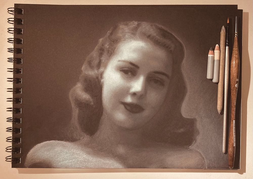 Disegno “fotorealistico” a matita su carta nera. Ritrae il volto di una giovane donna sorridente in tipico stile anni ‘50 (lo si desume soprattutto dalla capigliatura, dal trucco, dalla posa “classicamente finta” e dall’illuminazione tipicamente utilizzata nei film dell’epoca - tecnicamente “diva style” ovvero simil Rembrandt). Visivamente il volto (centrato) occupa 1/3 del foglio ancora attaccato al blocco sul quale sono appoggiate le matite, un pennello e uno sfumino di carta utilizzati per la sua realizzazione.