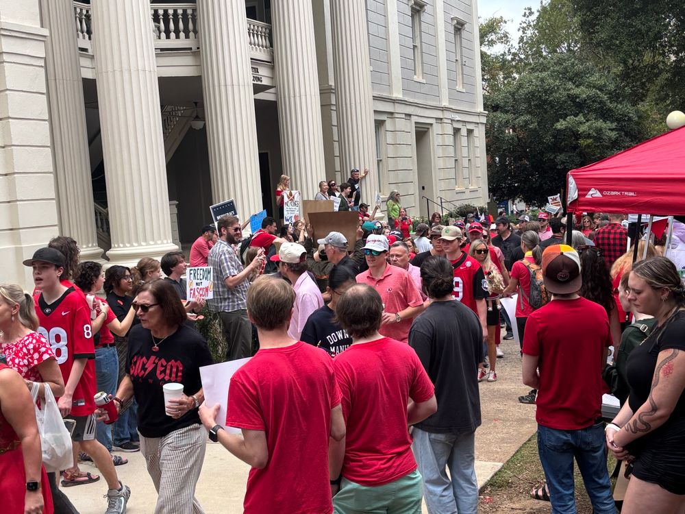 Crowd of No Kings protestors surrounding Georgia Bulldog football fans walking through the middle