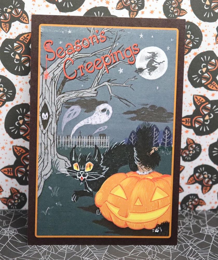 A vintage-style halloween postcard that reads "Season's Creepings" and features spooky imagery such as a black cat, a jack o lantern, and ghosts
