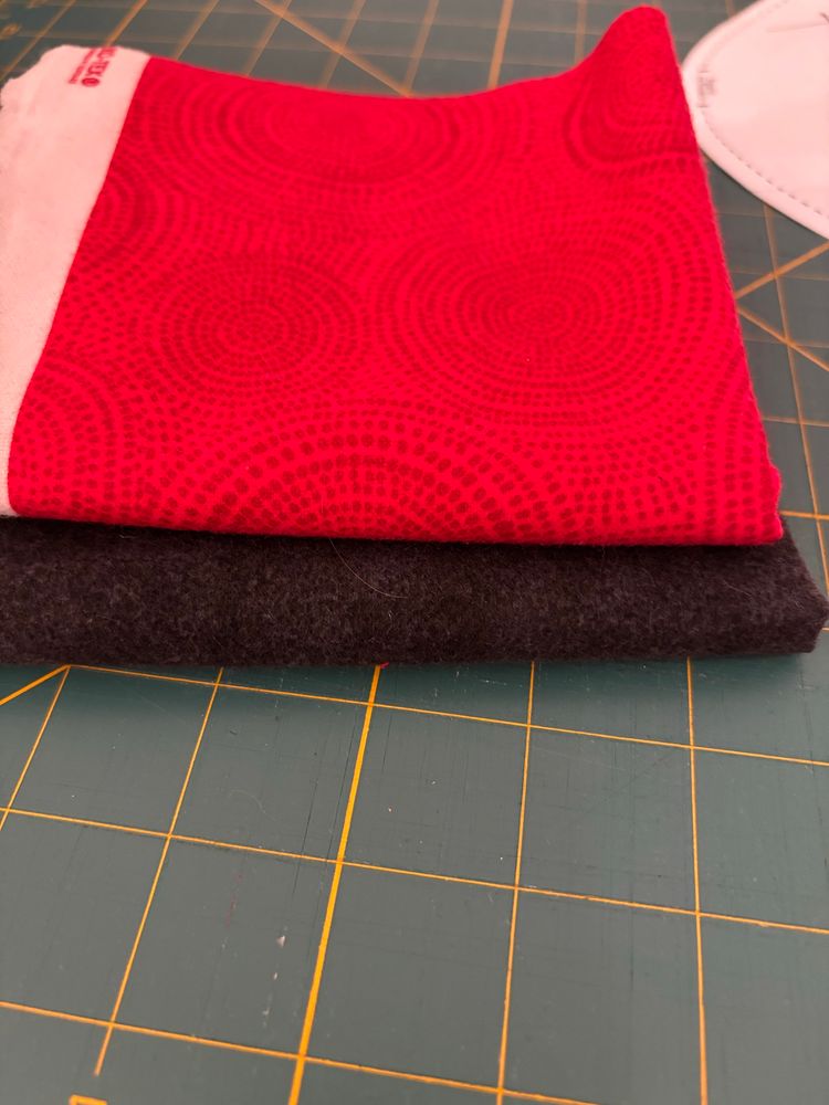 Two squares of folded fleece fabric, red and black, sitting on a cutting mat