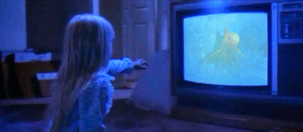 a little girl in a blue dress is looking at a television screen with a yellow octopus on it