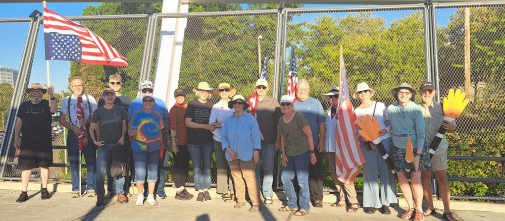 Row of people holding signs and US Flags on sidewalk of freeway overpass