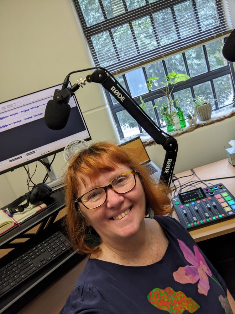 Kim has red hair and glassesand sits In front of some mircphones