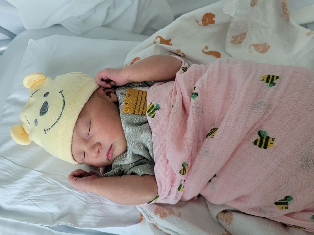 Newborn baby wrapped in a swaddle wearing a Winnie the pooh hat