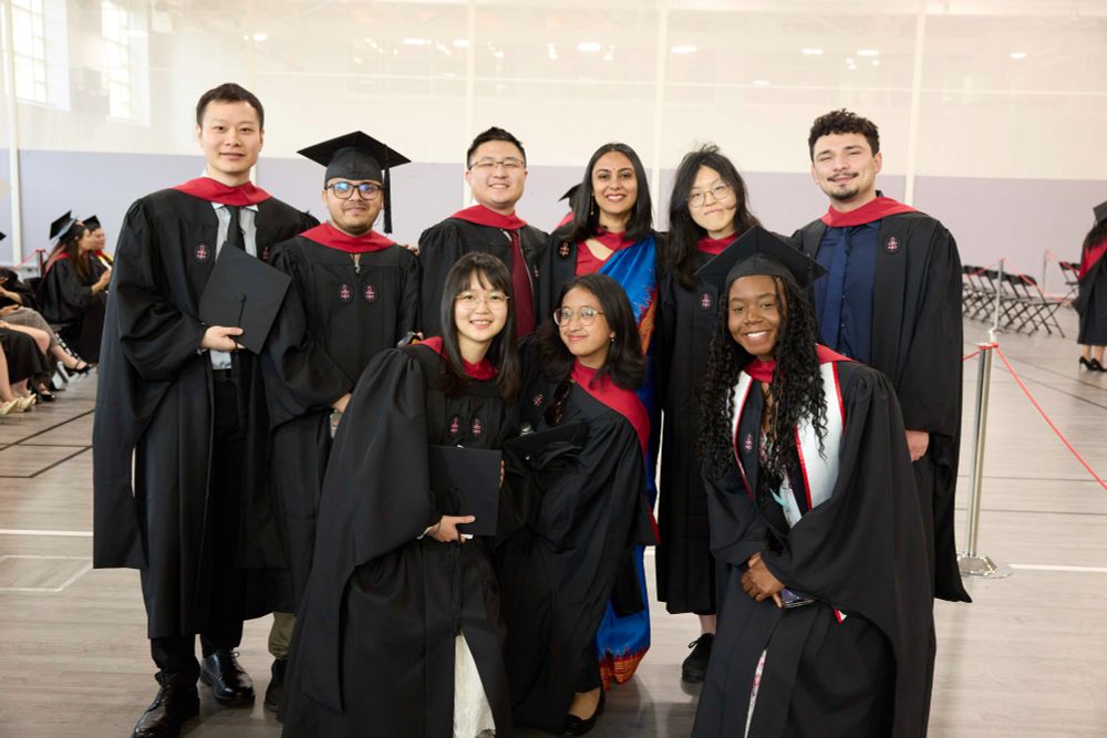 A group of nine graduates in black and red regalia, smiling.