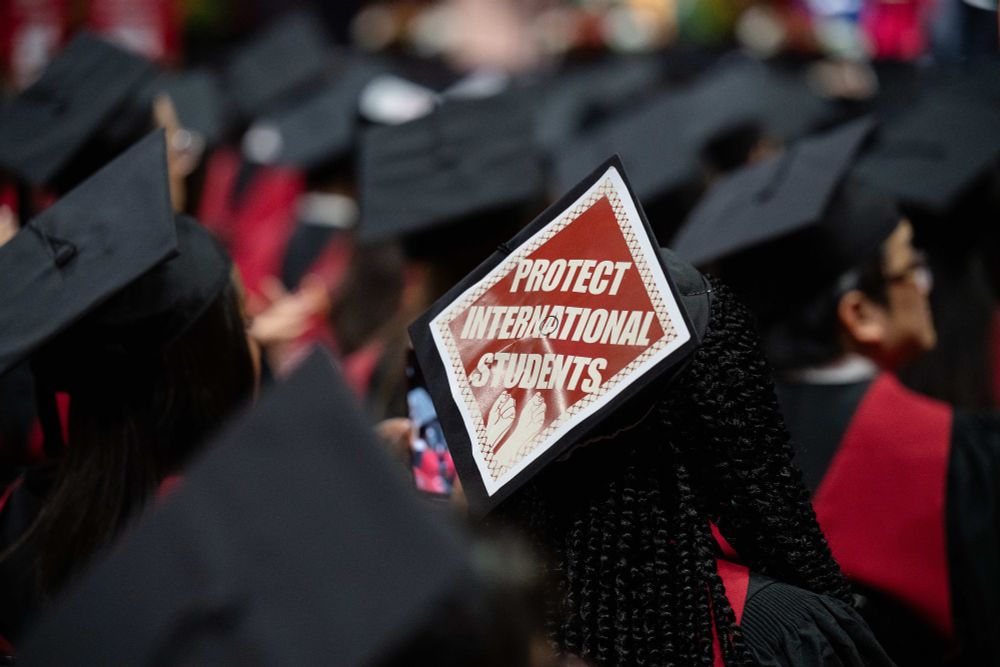 Graduation caps seen from behind with one cap featuring a sign that says "PROTECT INTERNATIONAL STUDENTS."