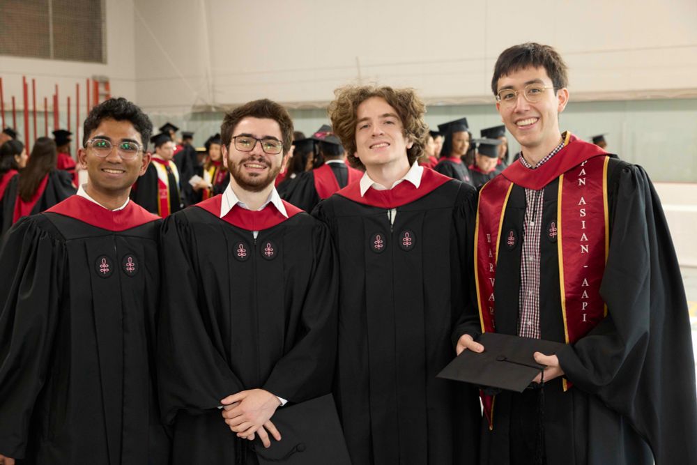 Four graduates wearing Harvard Chan School robes smile at the Convocation ceremony.