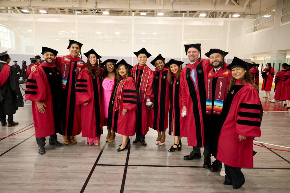Group of graduates in red and black academic regalia smiling.
