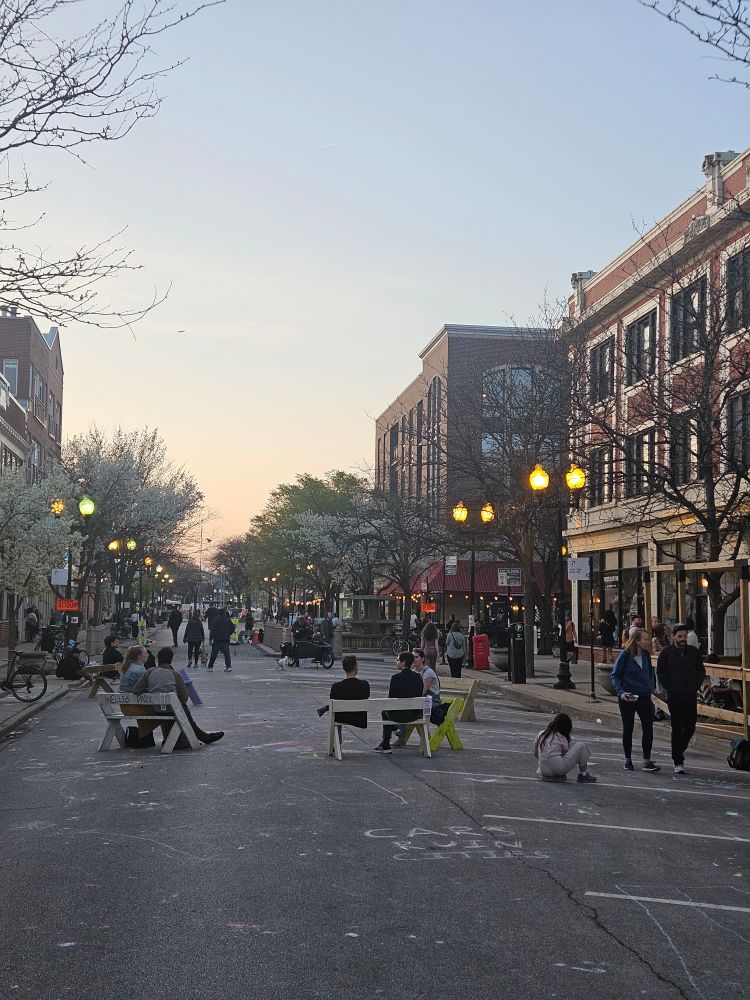 Photo of benches in the middle of a street with lots of people 