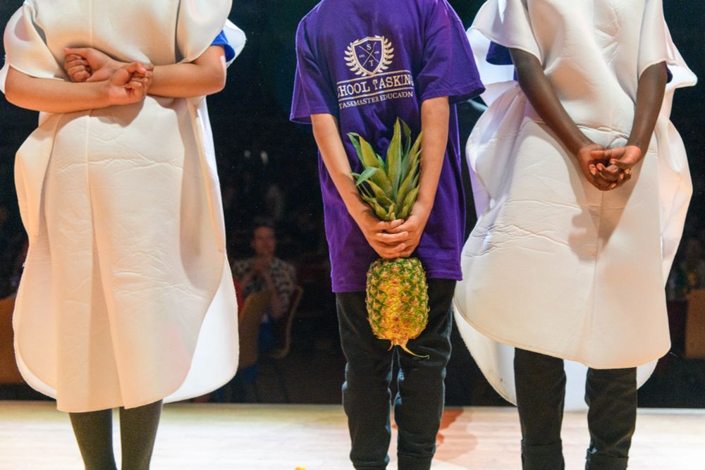 The backs of 3 children, one with a pineapple hidden.