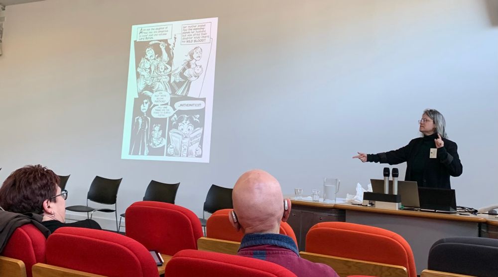 Sydney Padua speaking and gesturing; a b/w cartoon is on the screen