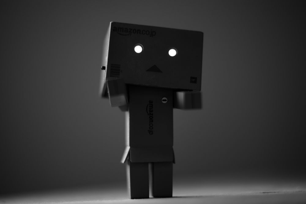 A monochromatic photograph of a fictional cardboard box robot character figurine called Danbo, with the eyes turned on, imitating a zombie.