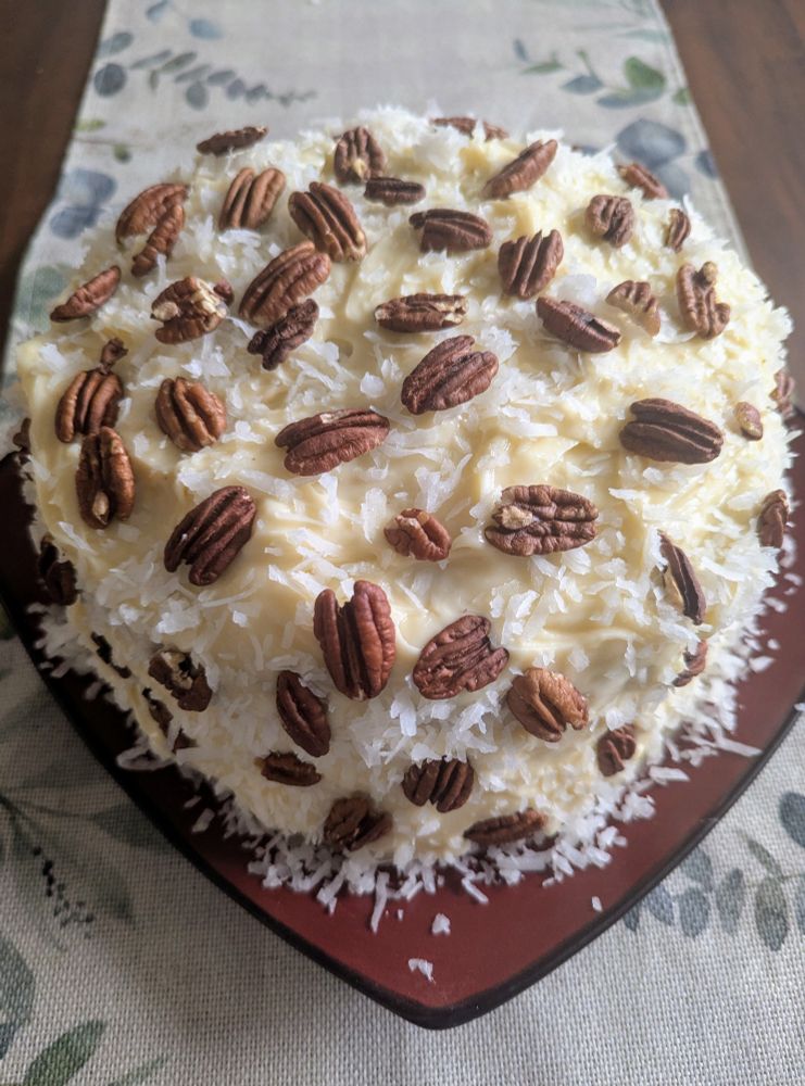 a hummingbird cake covered in pecans and coconut. icing is made from cream cheese