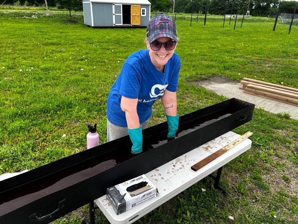 Woman dipping wood into long metal dip tank of stain 