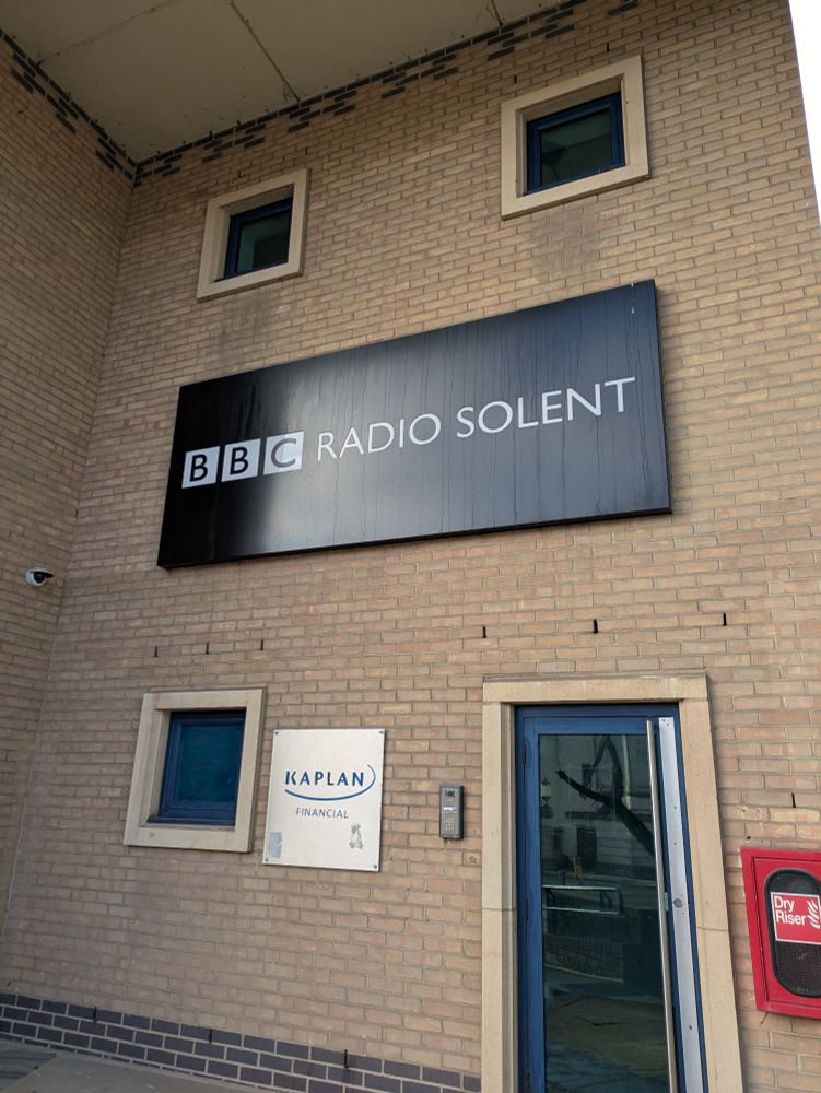 A photo of the outside of the BBC Southampton building with a big black sign on the wall that has the BBC Radio Solent logo on it.